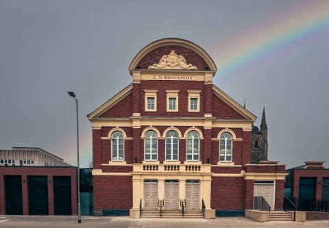 outside of an old theatre building with a rainbow in the sky